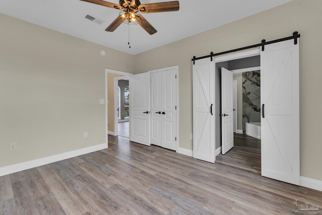 unfurnished bedroom with a closet, light hardwood / wood-style floors, a barn door, and ceiling fan