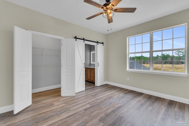 unfurnished bedroom featuring ensuite bath, light hardwood / wood-style flooring, ceiling fan, a barn door, and a closet