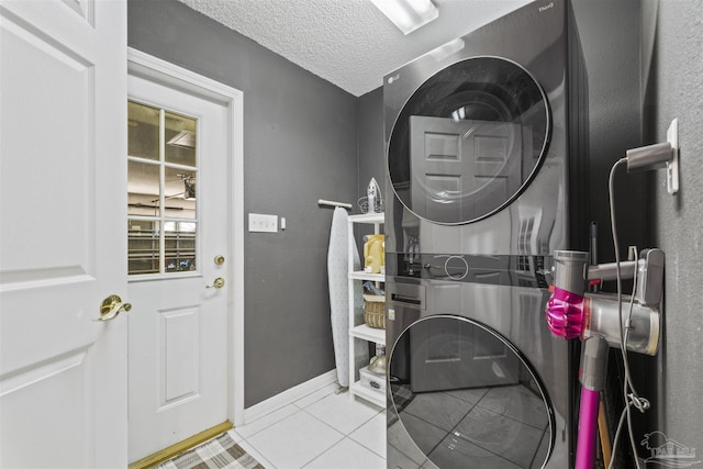 laundry area with stacked washer / dryer, a textured ceiling, tile patterned flooring, laundry area, and baseboards