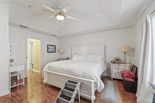 bedroom featuring a raised ceiling, visible vents, baseboards, and wood finished floors