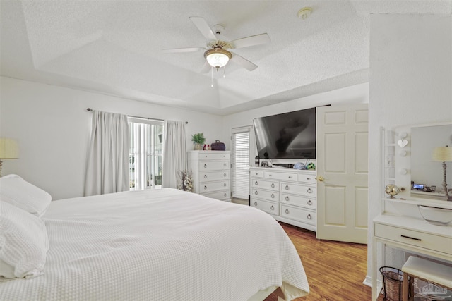 bedroom with a ceiling fan, a tray ceiling, a textured ceiling, and wood finished floors