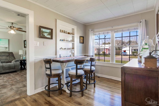 dining room featuring built in features, dark wood finished floors, baseboards, and ornamental molding