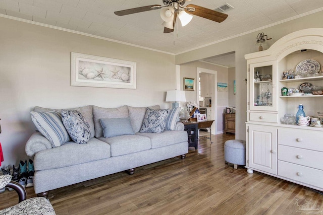 living room featuring ceiling fan, wood finished floors, visible vents, and crown molding