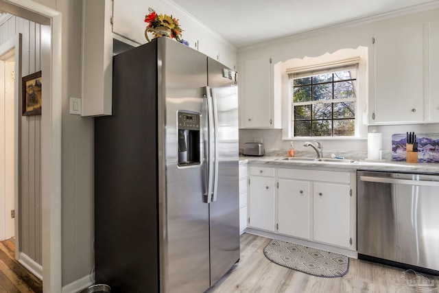 kitchen featuring a sink, light wood-style floors, light countertops, appliances with stainless steel finishes, and crown molding