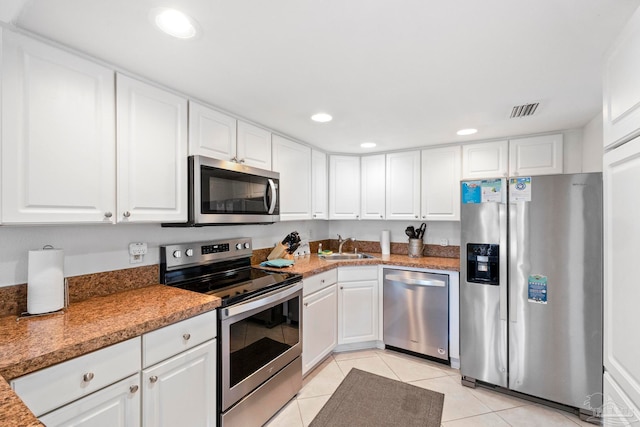 kitchen featuring stone counters, sink, stainless steel appliances, light tile patterned floors, and white cabinetry