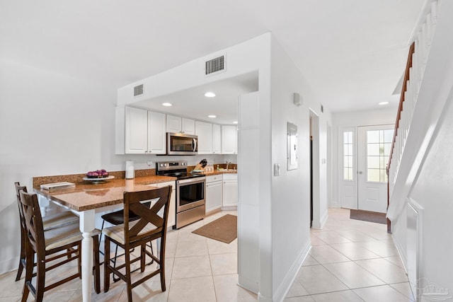 kitchen featuring white cabinets, kitchen peninsula, stone counters, appliances with stainless steel finishes, and a kitchen bar