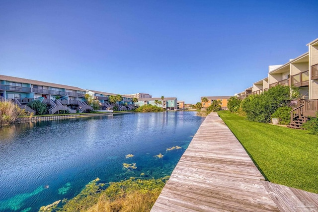 view of dock with a water view, a balcony, and a lawn