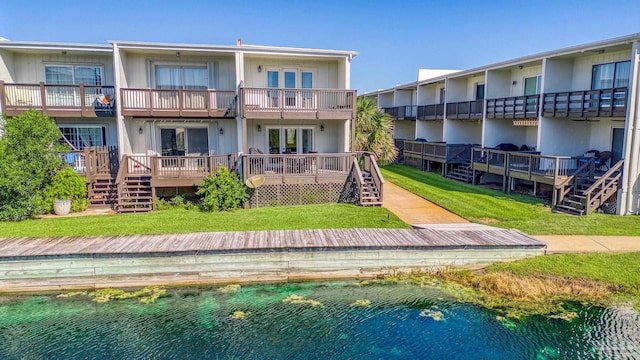 back of property with a deck with water view, a balcony, and a lawn