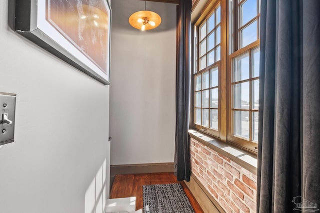 doorway with brick wall, baseboards, and wood finished floors