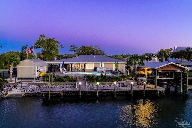 back house at dusk featuring an outbuilding and a water view