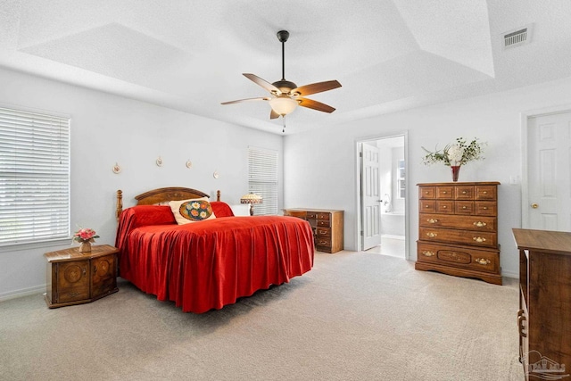 carpeted bedroom featuring a textured ceiling, ensuite bathroom, a raised ceiling, and ceiling fan