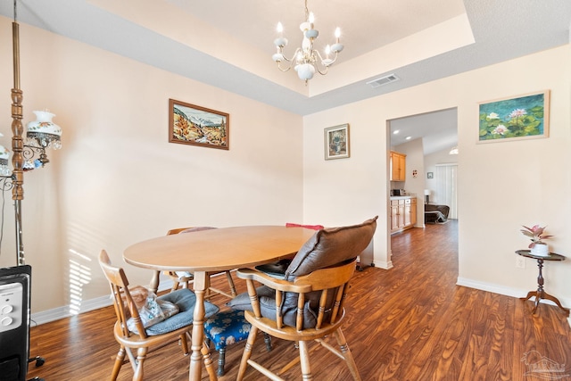 dining room with vaulted ceiling, a tray ceiling, an inviting chandelier, and dark wood-type flooring