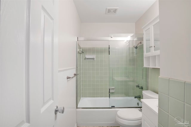 full bathroom featuring shower / bath combination with glass door, vanity, toilet, and tile walls