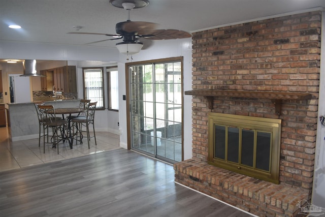 living room with baseboards, ceiling fan, a fireplace, and light wood finished floors