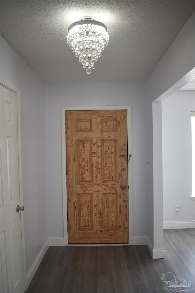 doorway to outside with a textured ceiling, baseboards, a notable chandelier, and wood finished floors