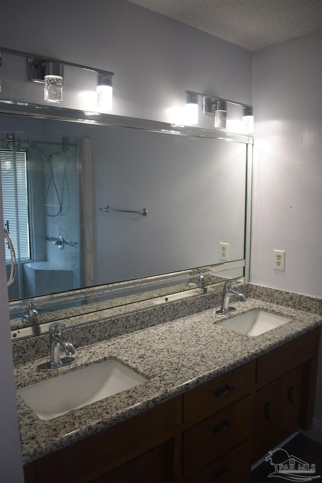 full bath featuring double vanity, a textured ceiling, a sink, and a stall shower