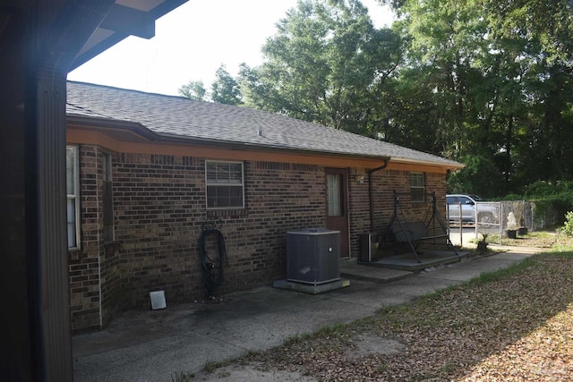exterior space featuring brick siding, roof with shingles, and central air condition unit