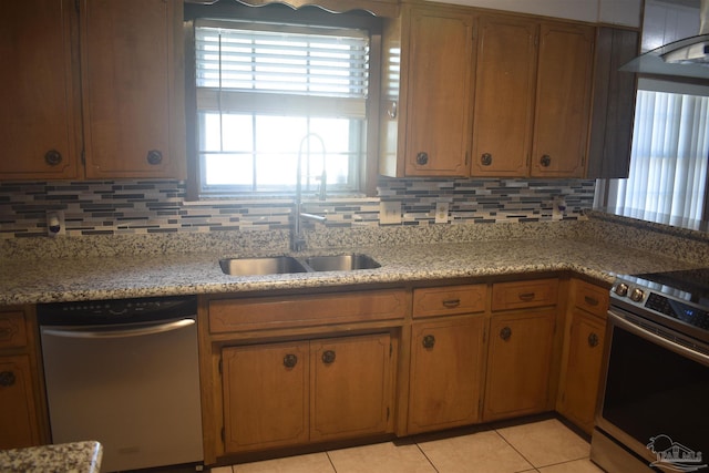 kitchen with appliances with stainless steel finishes, tasteful backsplash, brown cabinets, a sink, and light tile patterned floors