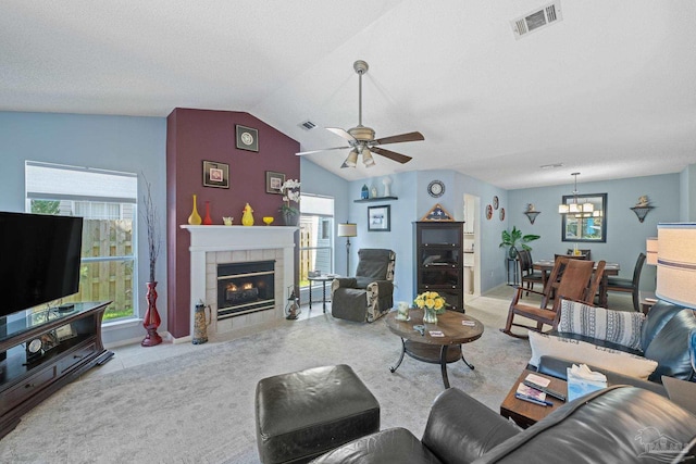 living room with a textured ceiling, lofted ceiling, ceiling fan with notable chandelier, and a tile fireplace