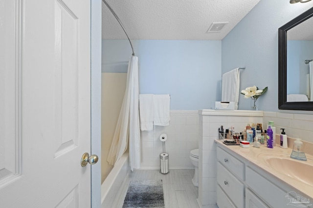 full bathroom featuring toilet, vanity, tile walls, shower / bath combo, and a textured ceiling