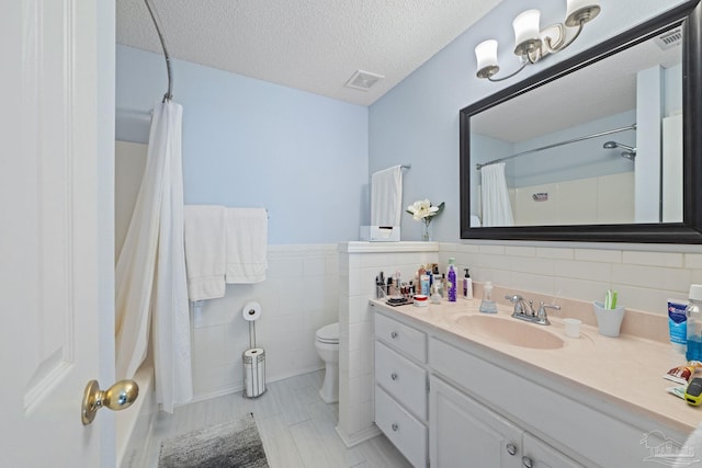 bathroom featuring a textured ceiling, toilet, tile walls, and vanity