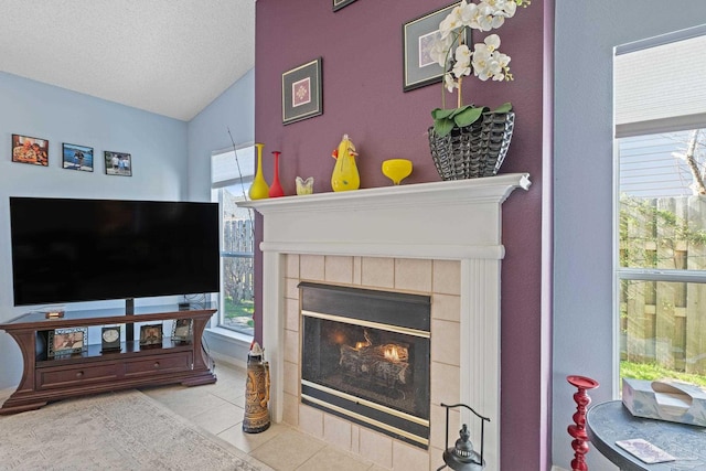 living room featuring lofted ceiling, light tile patterned floors, a tile fireplace, and a textured ceiling