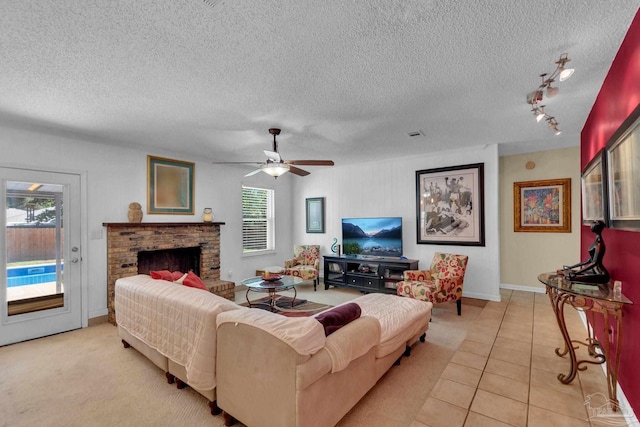 living room featuring a brick fireplace, a textured ceiling, ceiling fan, and light tile patterned floors