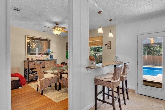 kitchen featuring light hardwood / wood-style floors, a textured ceiling, a breakfast bar area, ceiling fan, and pendant lighting