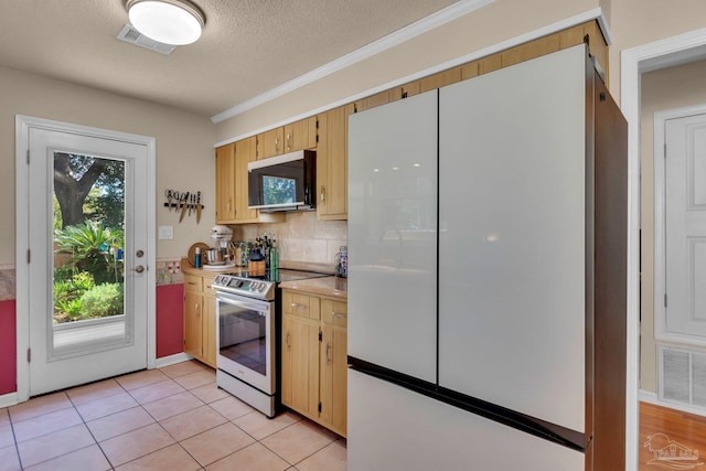 kitchen with appliances with stainless steel finishes, a textured ceiling, backsplash, and light tile patterned floors