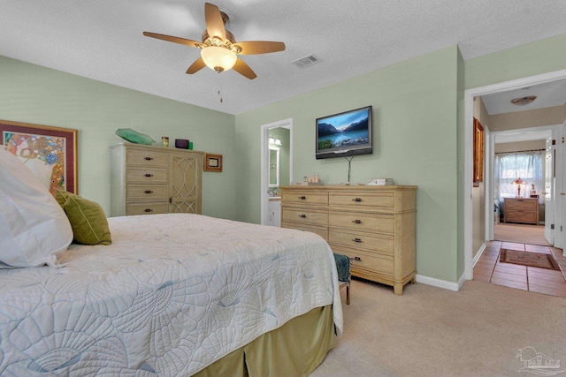 bedroom featuring ensuite bathroom, ceiling fan, a textured ceiling, and light colored carpet