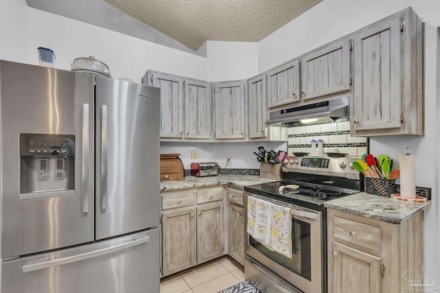 kitchen featuring stainless steel appliances, a textured ceiling, light tile patterned floors, light brown cabinetry, and light stone counters