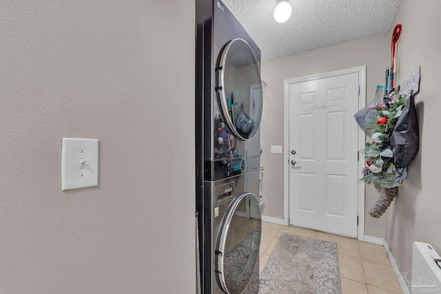 laundry area with a textured ceiling, light tile patterned floors, and stacked washer / dryer