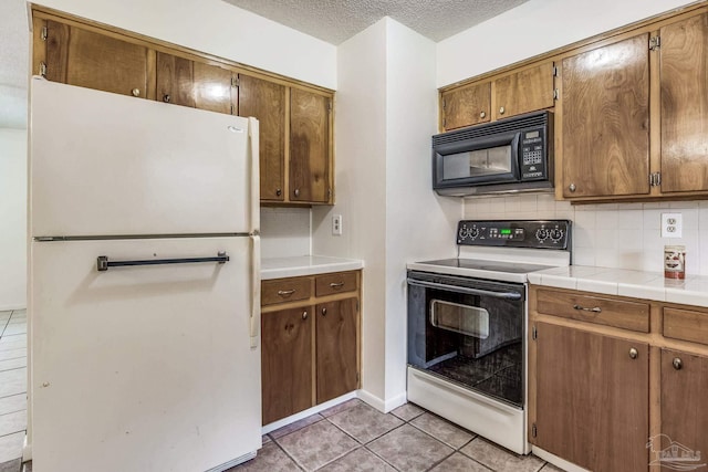 kitchen featuring tile counters, a textured ceiling, tasteful backsplash, light tile patterned flooring, and white appliances