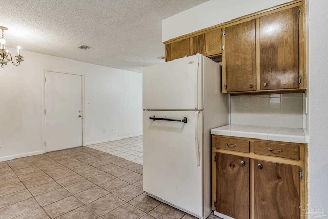 kitchen featuring white refrigerator, tile counters, light tile patterned floors, and a textured ceiling