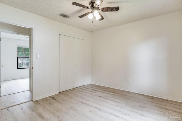 unfurnished bedroom featuring ceiling fan, a textured ceiling, a closet, and light wood-type flooring