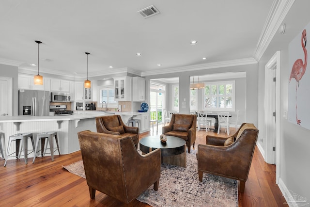 living room featuring ornamental molding, sink, and light hardwood / wood-style floors