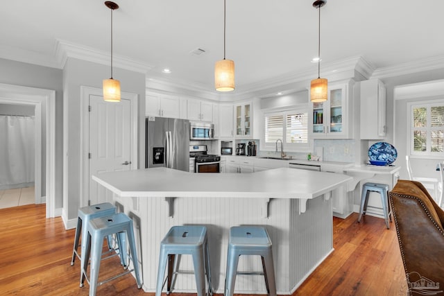 kitchen featuring a breakfast bar, sink, pendant lighting, stainless steel appliances, and white cabinets