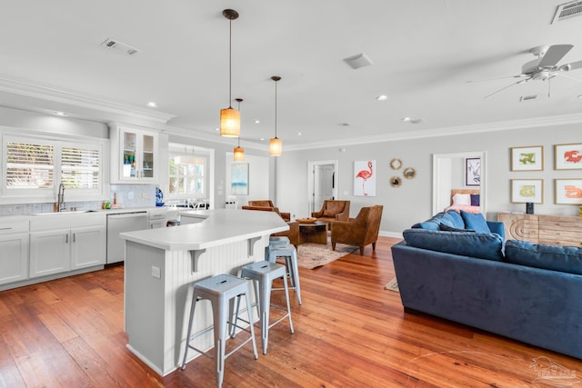 kitchen featuring a kitchen bar, sink, white cabinetry, decorative light fixtures, and dishwasher