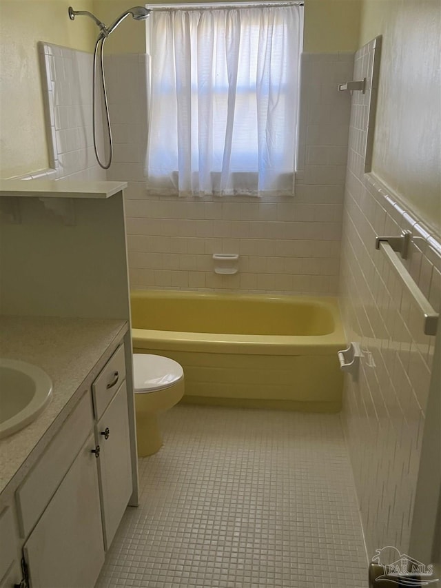 bathroom featuring toilet, tile walls, washtub / shower combination, tile patterned flooring, and vanity