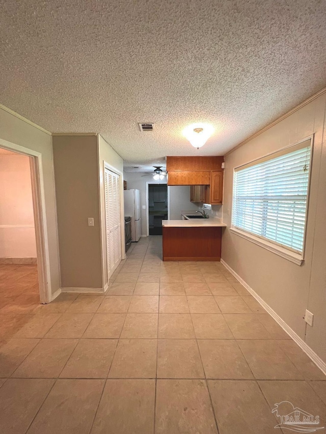 kitchen featuring white fridge, a textured ceiling, light tile patterned floors, sink, and kitchen peninsula