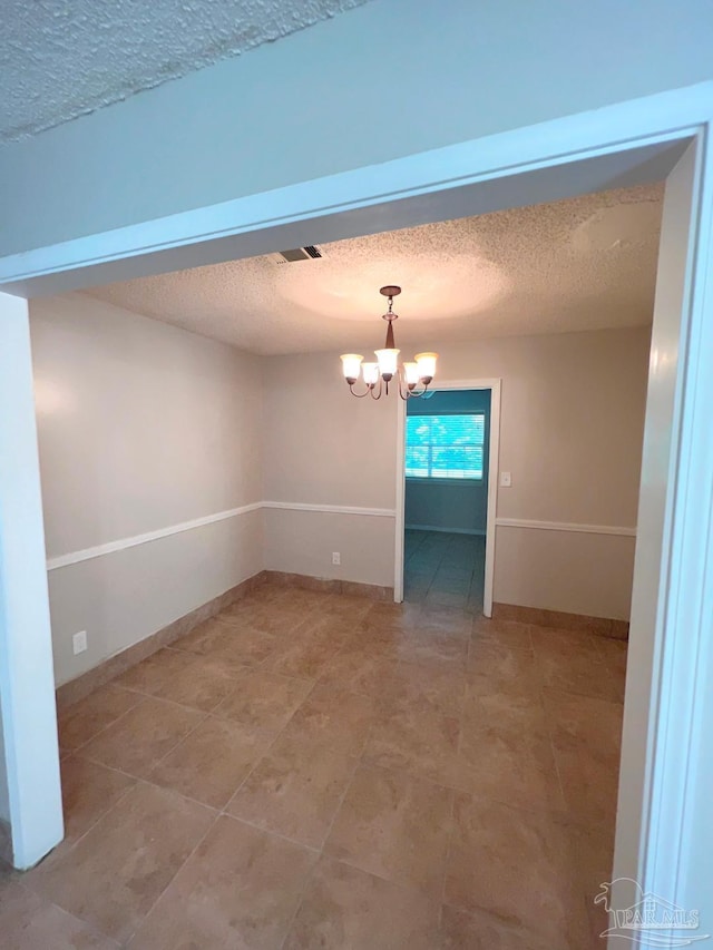 tiled spare room with a textured ceiling and an inviting chandelier