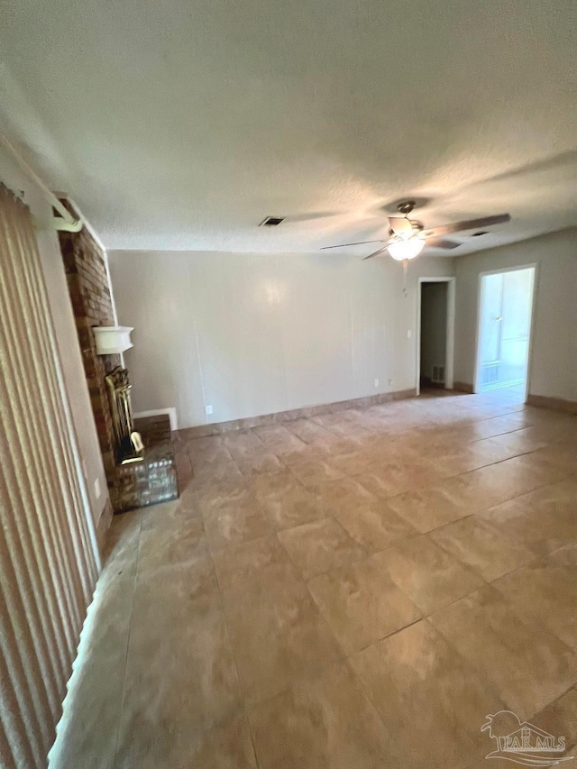 unfurnished room with a textured ceiling, ceiling fan, and a fireplace