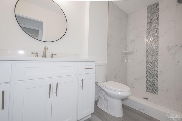 bathroom with hardwood / wood-style flooring, vanity, a tile shower, and toilet