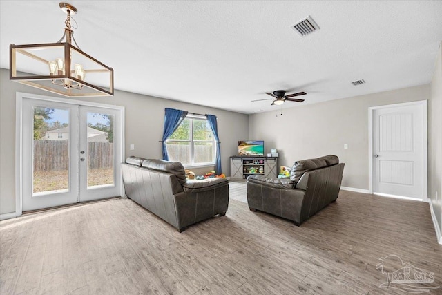 living room with french doors, ceiling fan with notable chandelier, hardwood / wood-style floors, and a textured ceiling