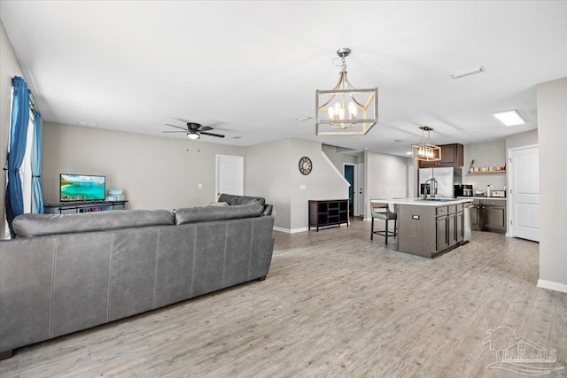 living room featuring sink, ceiling fan with notable chandelier, and light wood-type flooring