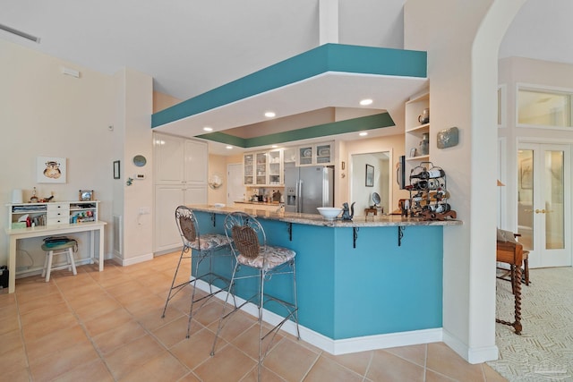 kitchen featuring kitchen peninsula, french doors, stainless steel fridge with ice dispenser, white cabinetry, and a breakfast bar area