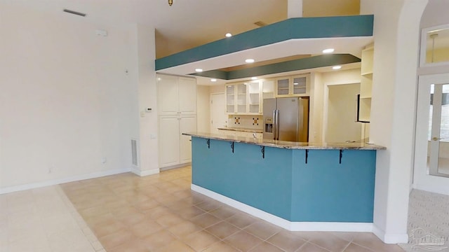 1129 Seabreeze Ln, Gulf Breeze, FL 32563 - kitchen with light stone counters, stainless steel fridge with ice dispenser, a breakfast bar, a peninsula, and glass insert cabinets