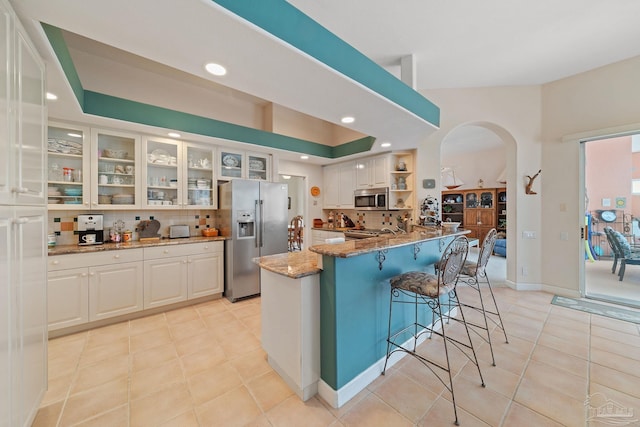 kitchen featuring decorative backsplash, stainless steel appliances, white cabinetry, and light stone counters