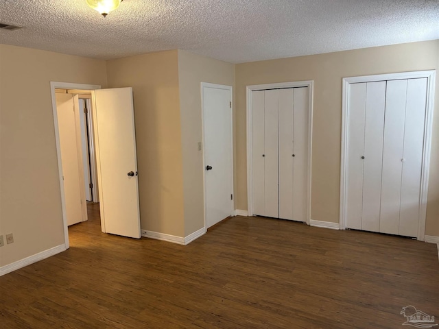 unfurnished bedroom with visible vents, baseboards, dark wood-style flooring, a textured ceiling, and two closets