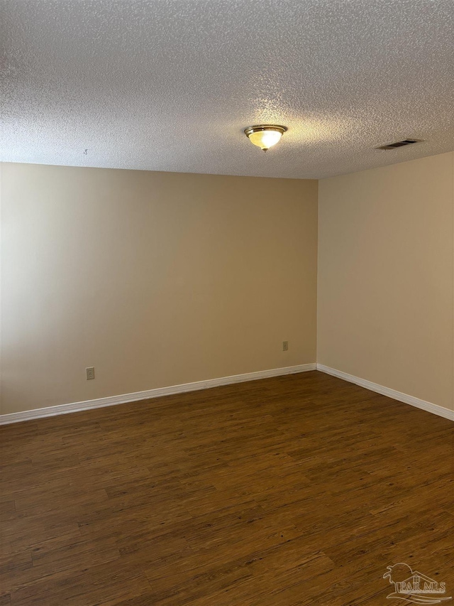 spare room with dark wood finished floors, visible vents, a textured ceiling, and baseboards